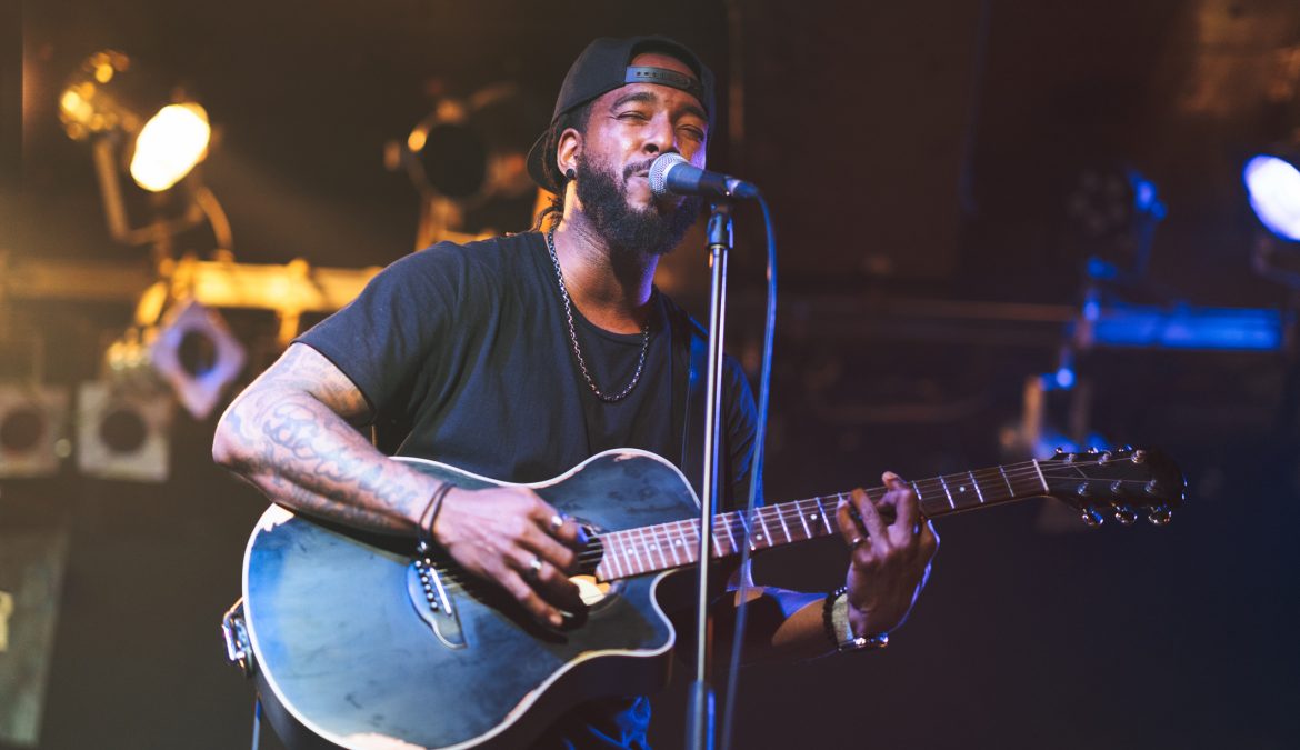 Black man playing acoustic guitar and singing on stage